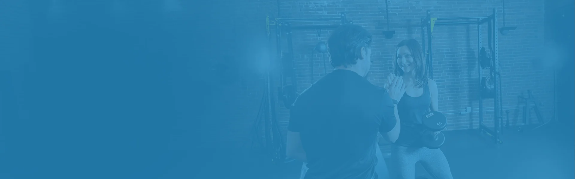 Two men are in a gym; one is using a rowing machine while the other, possibly a trainer, gives encouragement and guidance.