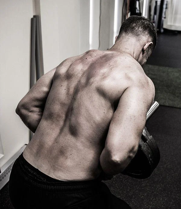 satrength-1 A muscular man with a bare back performs a bent-over row exercise with a dumbbell in a gym setting.
