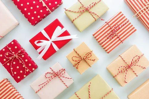 Assorted gift boxes wrapped in red, white, and brown paper with string and ribbon, arranged neatly on a white surface.
