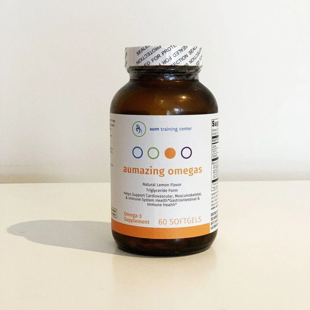 aumazingomegas_website (1) A brown bottle labeled "aumazing omegas" omega-3 supplement with 60 softgels, sealed with a safety wrapper, standing on a white surface.