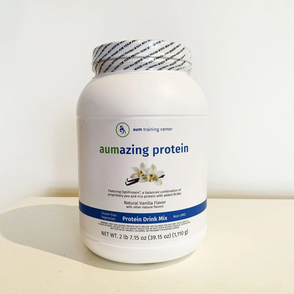 A white container of aum training center’s aumazing protein drink mix in natural vanilla flavor, with information about ingredients and weight on the label.