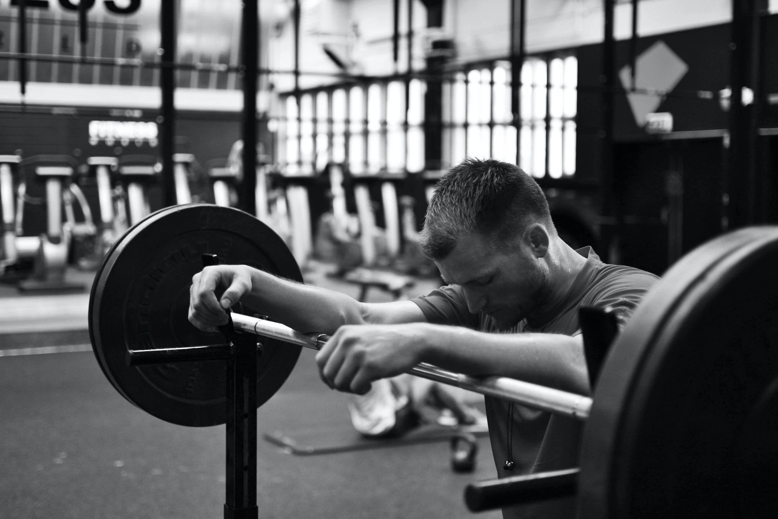image-asset A person rests their head and arms on a barbell in a gym, appearing fatigued after lifting weights. Gym equipment is visible in the background.