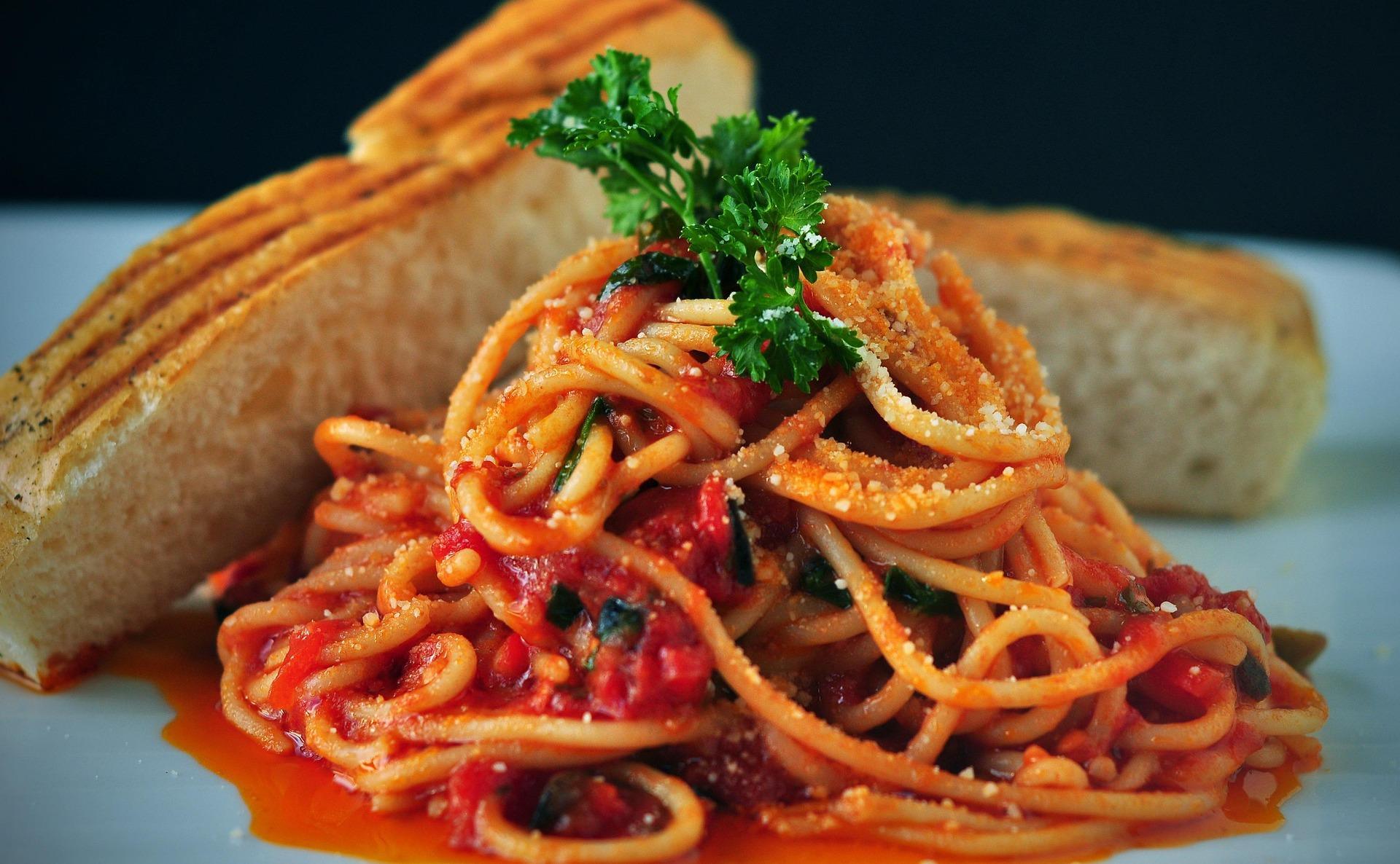 A plate of spaghetti with tomato sauce, garnished with parsley and grated cheese, served with two slices of grilled bread—perfect for refueling after a session with your Boston personal trainer.
