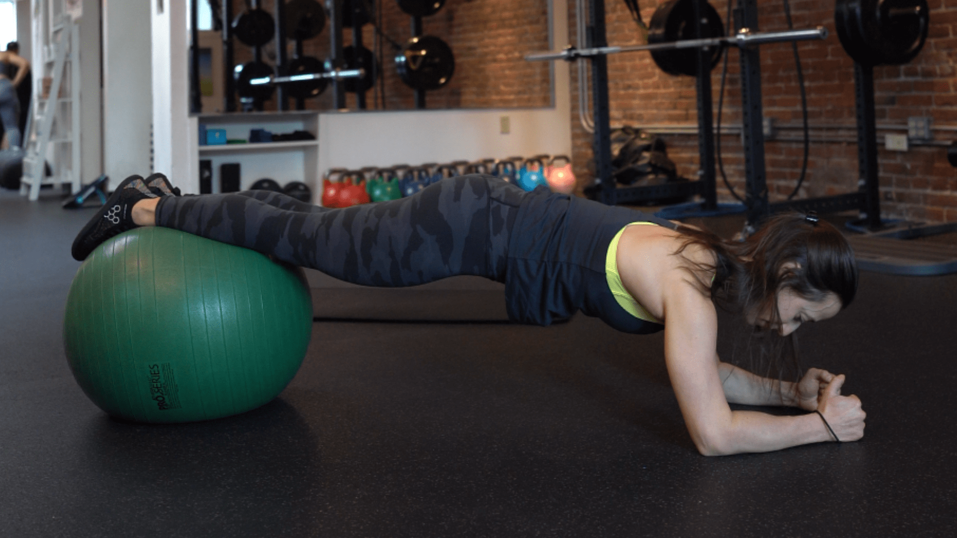 A woman performs a plank exercise with her legs resting on a large green stability ball in a gym setting, showcasing core strength during personal training Boston sessions.