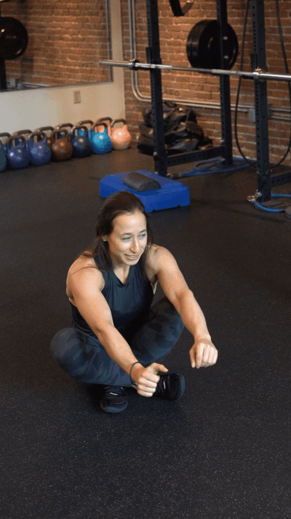 A person in athletic wear performs a seated single-leg squat exercise in a gym with kettlebells and weightlifting equipment, showcasing the focused atmosphere of Boston personal training.