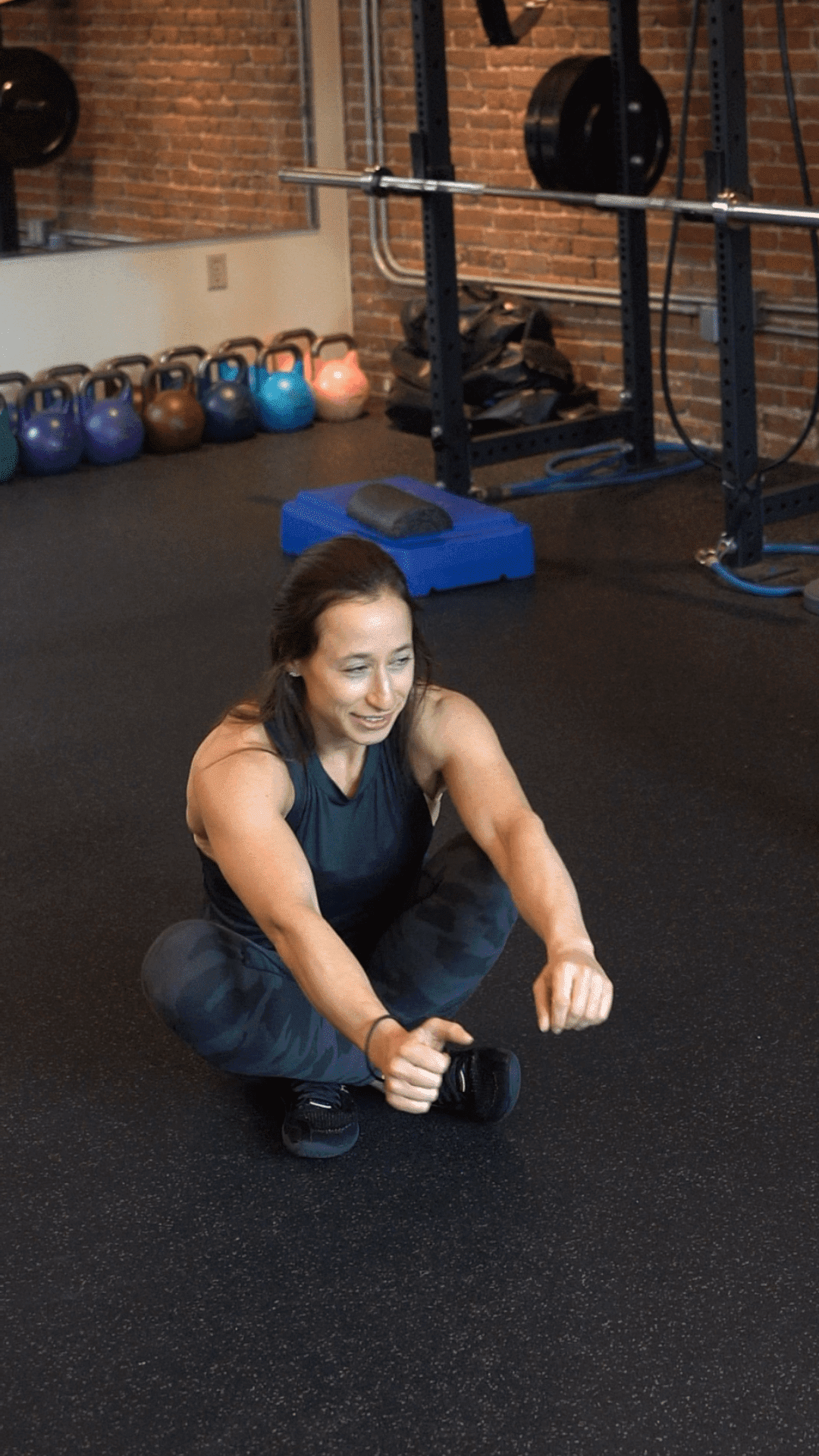 A person in athletic wear performs a seated single-leg squat exercise in a gym with kettlebells and weightlifting equipment, showcasing the focused atmosphere of Boston personal training.