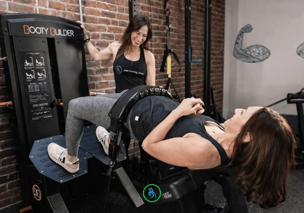 ‘Aum’ is a sacred sound that is known generally as the sound of the universe. Om is all encompassing, the essence of ultimate reality, and unifies everything in the universe. (1000 x 700 px) (3) copy Two women in workout attire use a hip thrust machine called Booty Builder in a gym with brick walls and fitness-themed wall art.