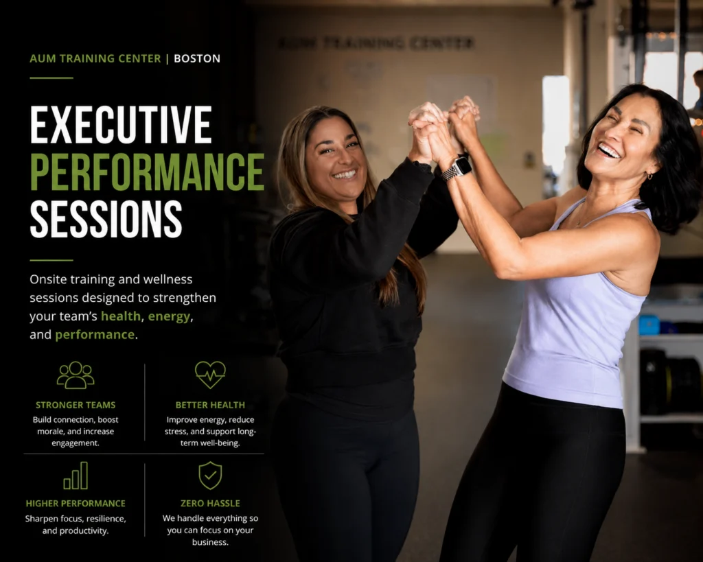 Two women smiling and high-fiving in a gym setting near fitness equipment, promoting executive performance sessions at AUM Training Center in Boston.