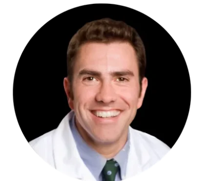 Dr. Joseph F. Merola Smiling man wearing a white lab coat and green tie, shown from the shoulders up against a black circular background, exuding the confident demeanor of a dedicated Boston Personal Trainer.